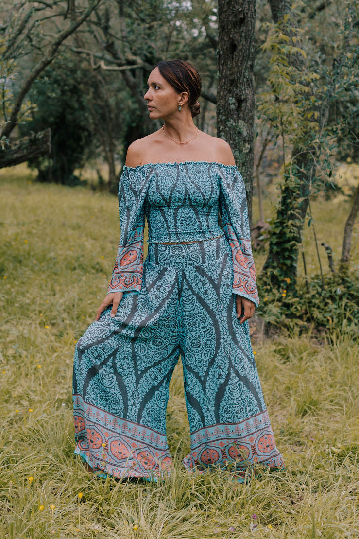 completo estivo boho chic da donna in viscosa  fresca e leggera azzurro turchese il completo è composto da un top arricciato con maniche lunghe e da un pantalone scampanato effetto panta gonna foto frontale ambientata in un bosco incantato lapeapois