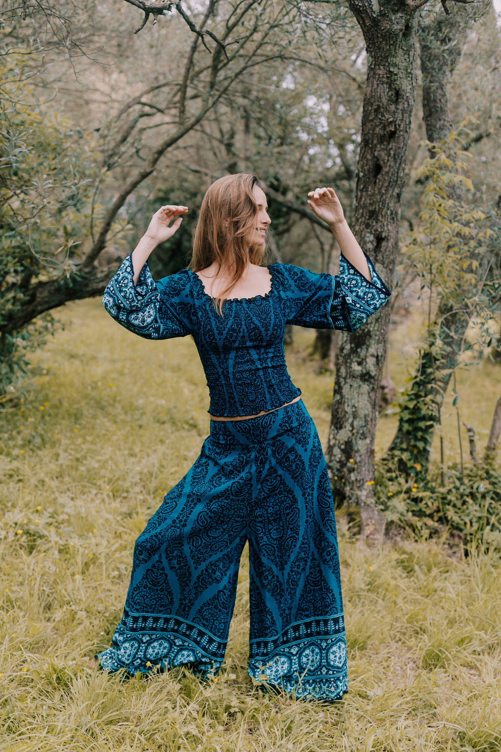 completo estivo donna boho chic ibiza style in viscosa fresca e leggera dalla stampa blu petrolio composto da top arricciato manica lunga e pantalone palazzo dalla gamba ampia e scampanata indossato da fata bionda in un bosco incantato lapeapois